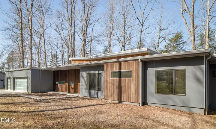 Photo of a long modern house with wood and grey panel siding among bare trees