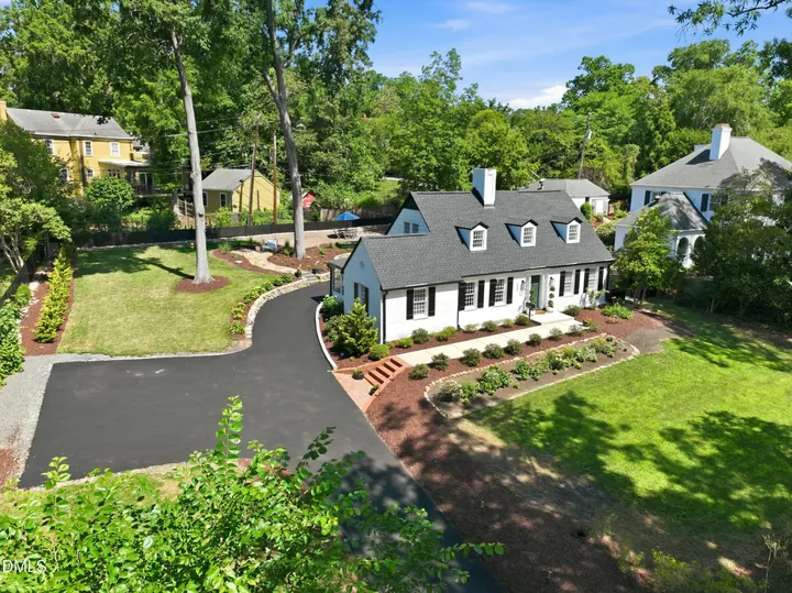 Aerial photo of a white brick Cape Cod with three dormers and black shutters